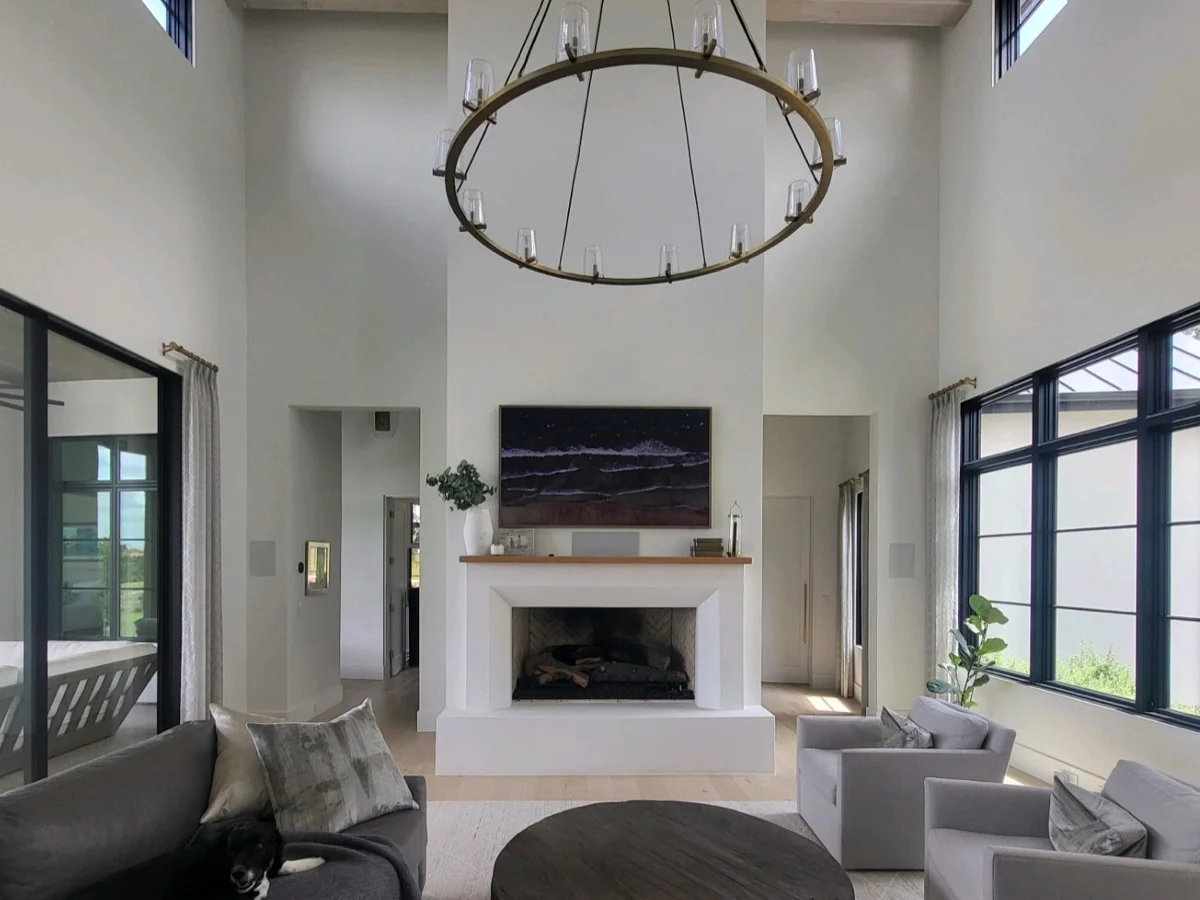 An open-plan Austin living room with a wall-mounted display over a fireplace, architectural speakers, and a statement chandelier, by AV Connect