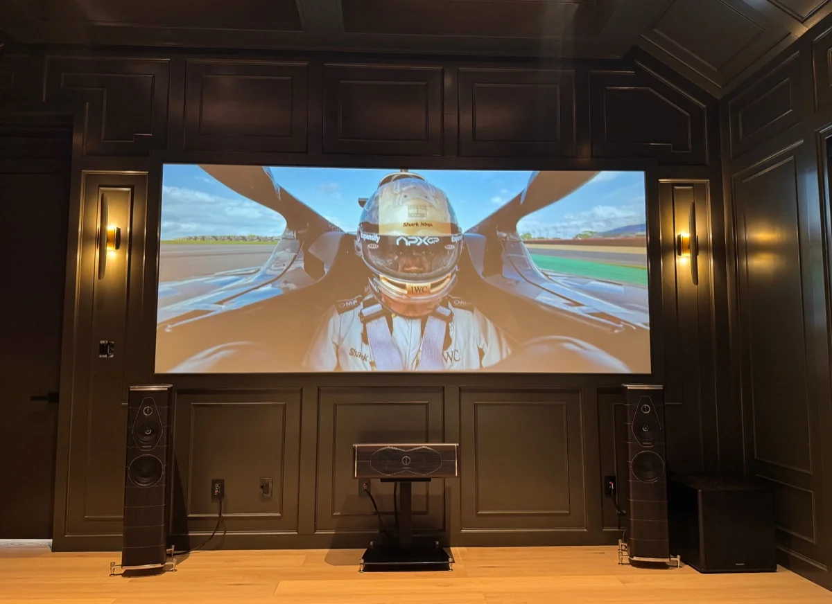 A dedicated media room with a wide projection screen, tower speakers, and dark wood paneling in an Austin, TX home