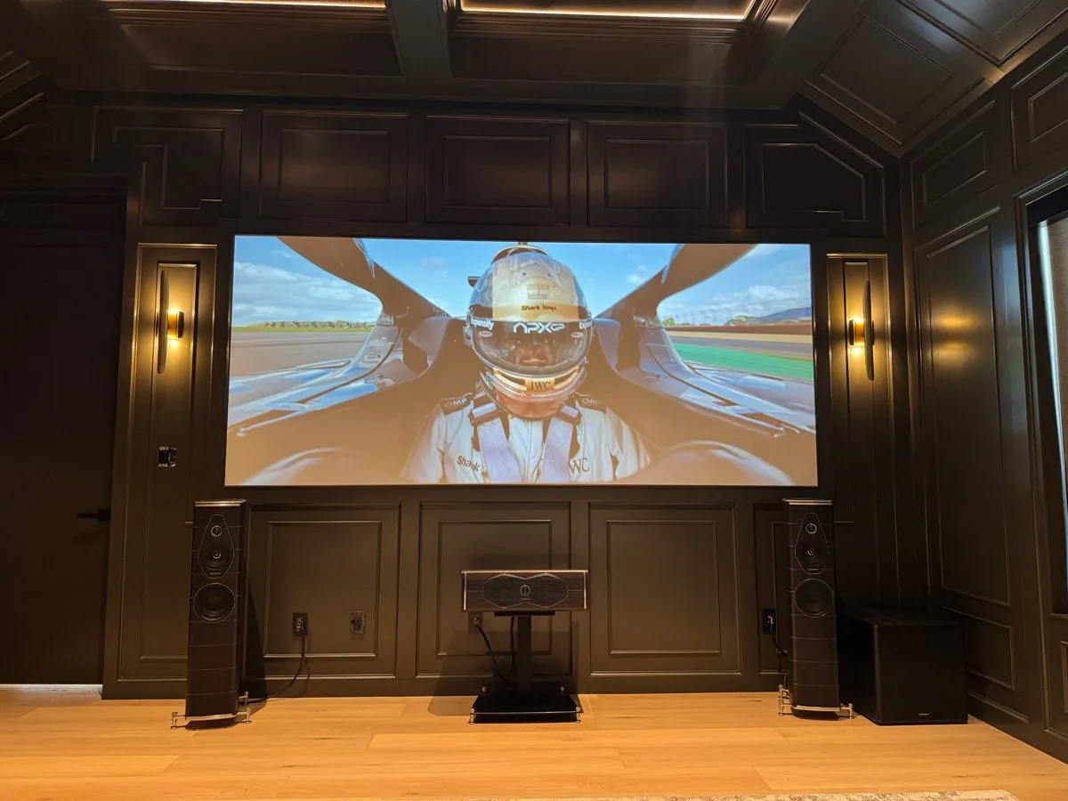 Calibrated projection screen framed by sconces and tower speakers in a paneled theater. Theater calibration for West Lake Hills, TX homes by AV Connect.