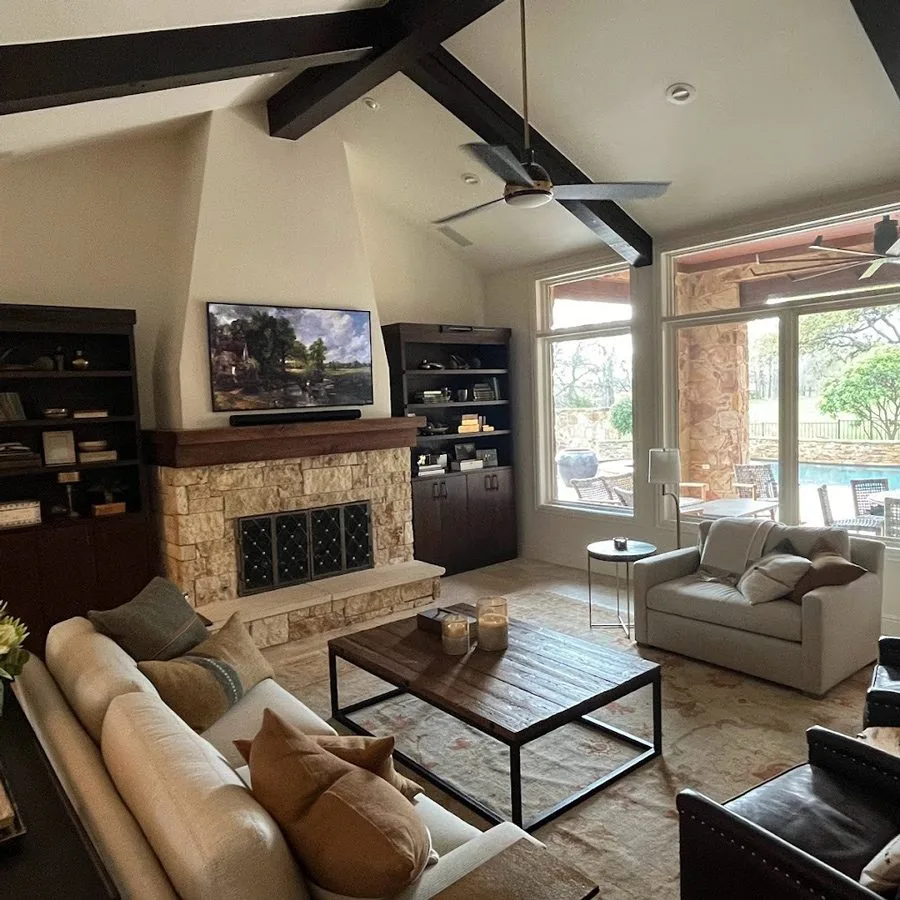 Living room with a TV above a stone fireplace and windows overlooking the pool, an example of the smart home automation AV Connect provides for Lakeway, TX homes.
