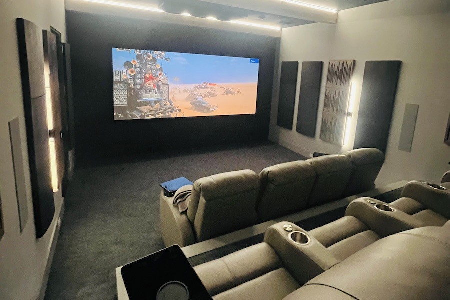 a projection screen shows a movie scene in a beige-colored home theater space with recliner chairs.
