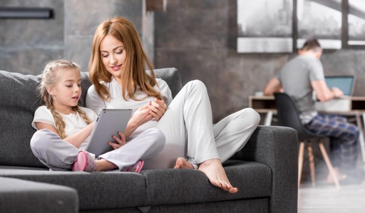 a family enjoys fast home networking in austin, with a mother and daughter using a tablet and a father on a laptop in the background.