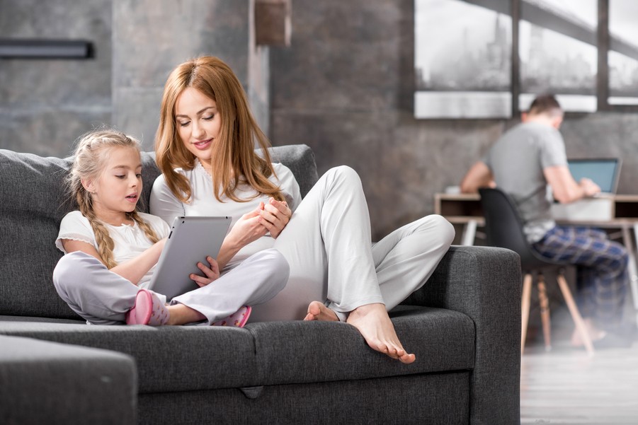 a family enjoys fast home networking in austin, with a mother and daughter using a tablet and a father on a laptop in the background.