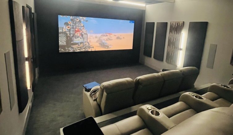 a projection screen shows a movie scene in a beige colored home theater space with recliner chairs.