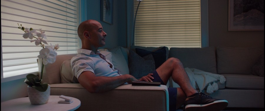 man lounging on a couch next to a lutron pico remote on a coffee table. automated blinds are lowered in the background.