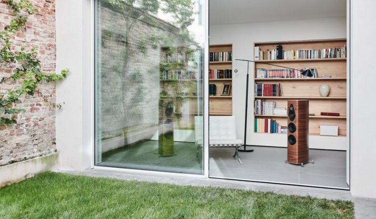 a modern home in austin with large glass doors revealing a wooden bookshelf and a pair of high end audio speakers.